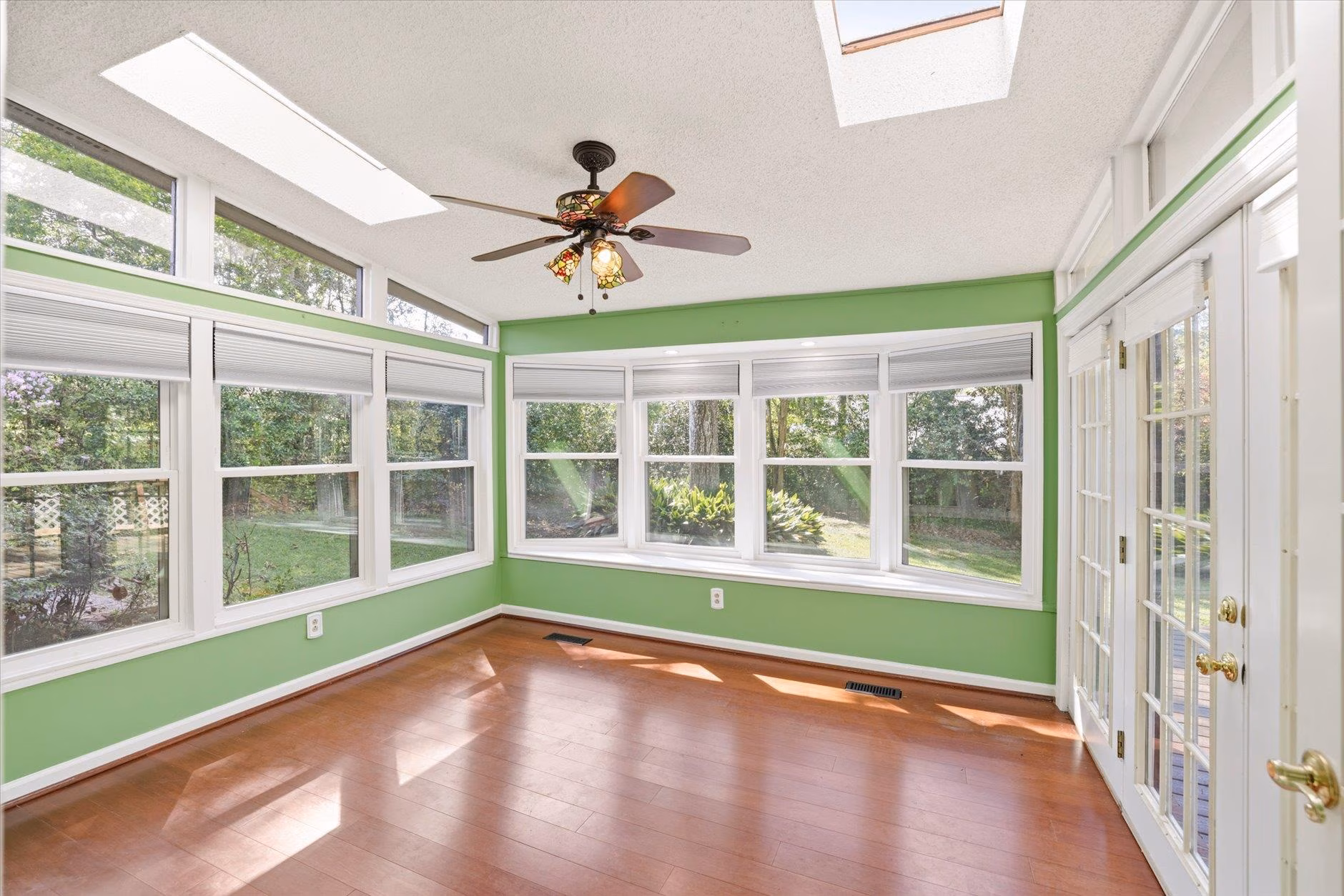 Bright sunroom with green walls and wooden floors.