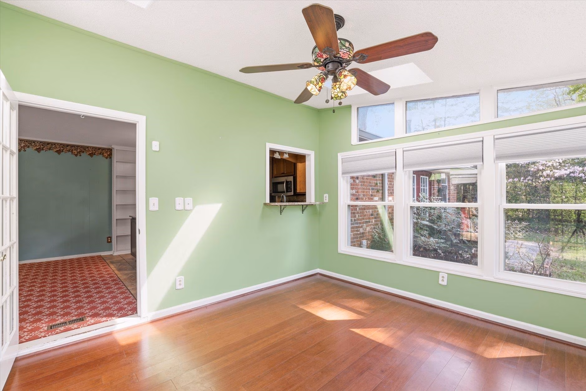 Bright empty room with green walls, large windows, and wooden floors.