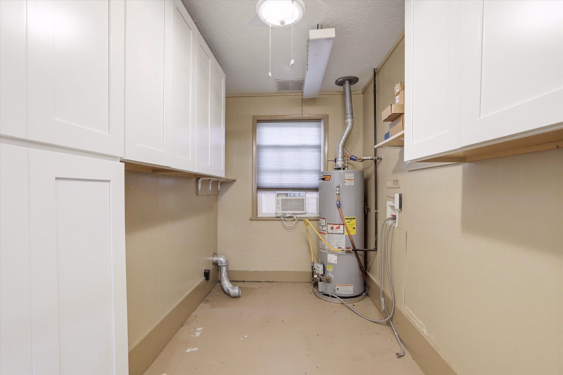 A clean utility room with a water heater and white cabinets.