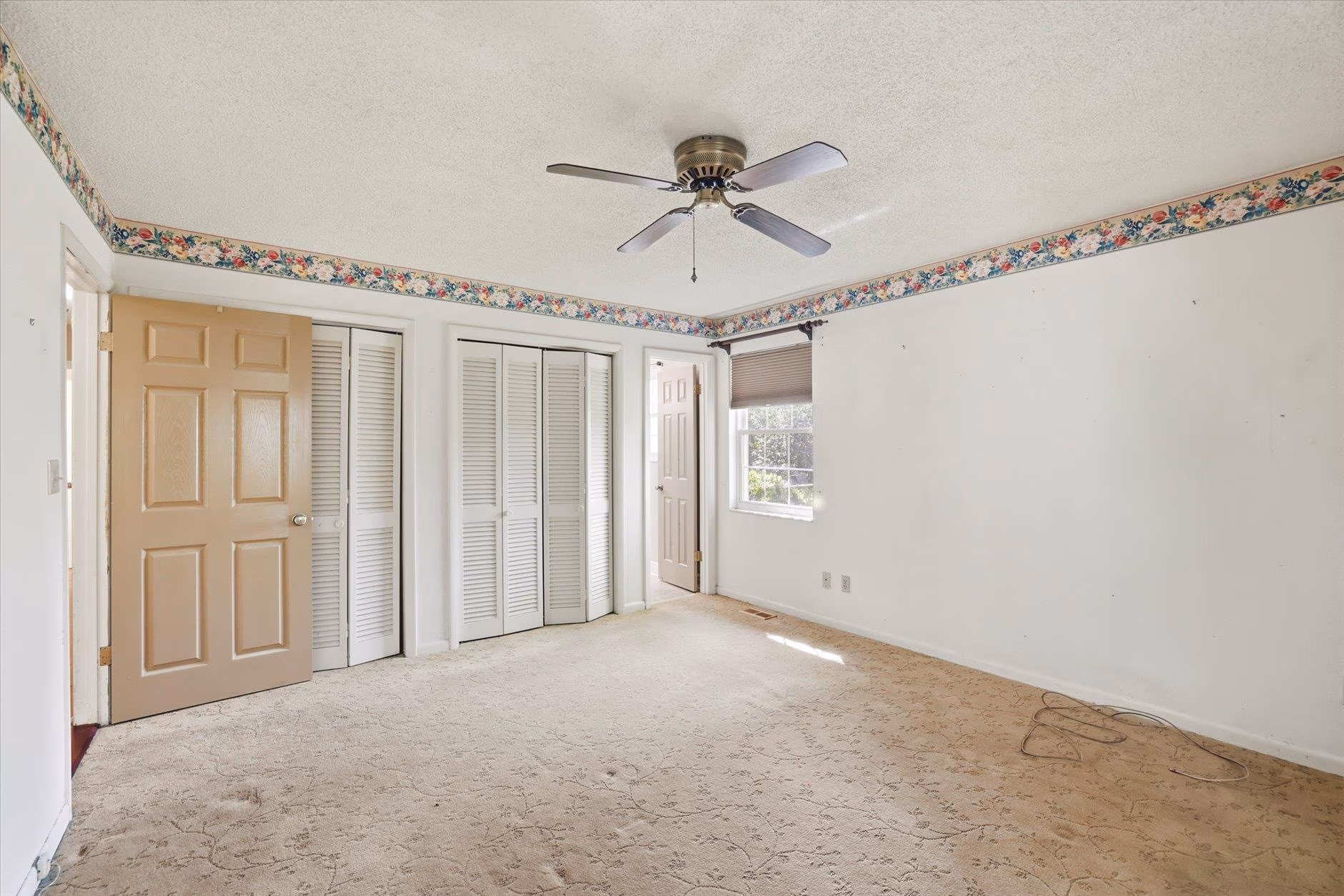 Empty bedroom with beige carpet, ceiling fan, and white closet doors.
