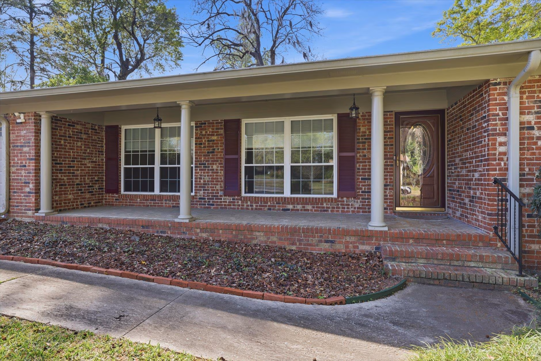 Front porch of a house with brick pillars and large windows.