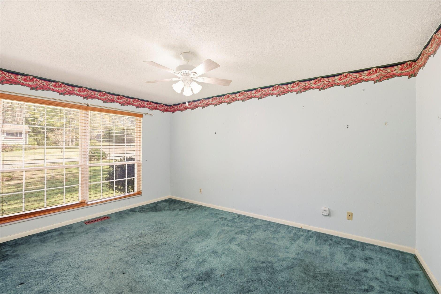 Empty bedroom with green carpet and ceiling fan.