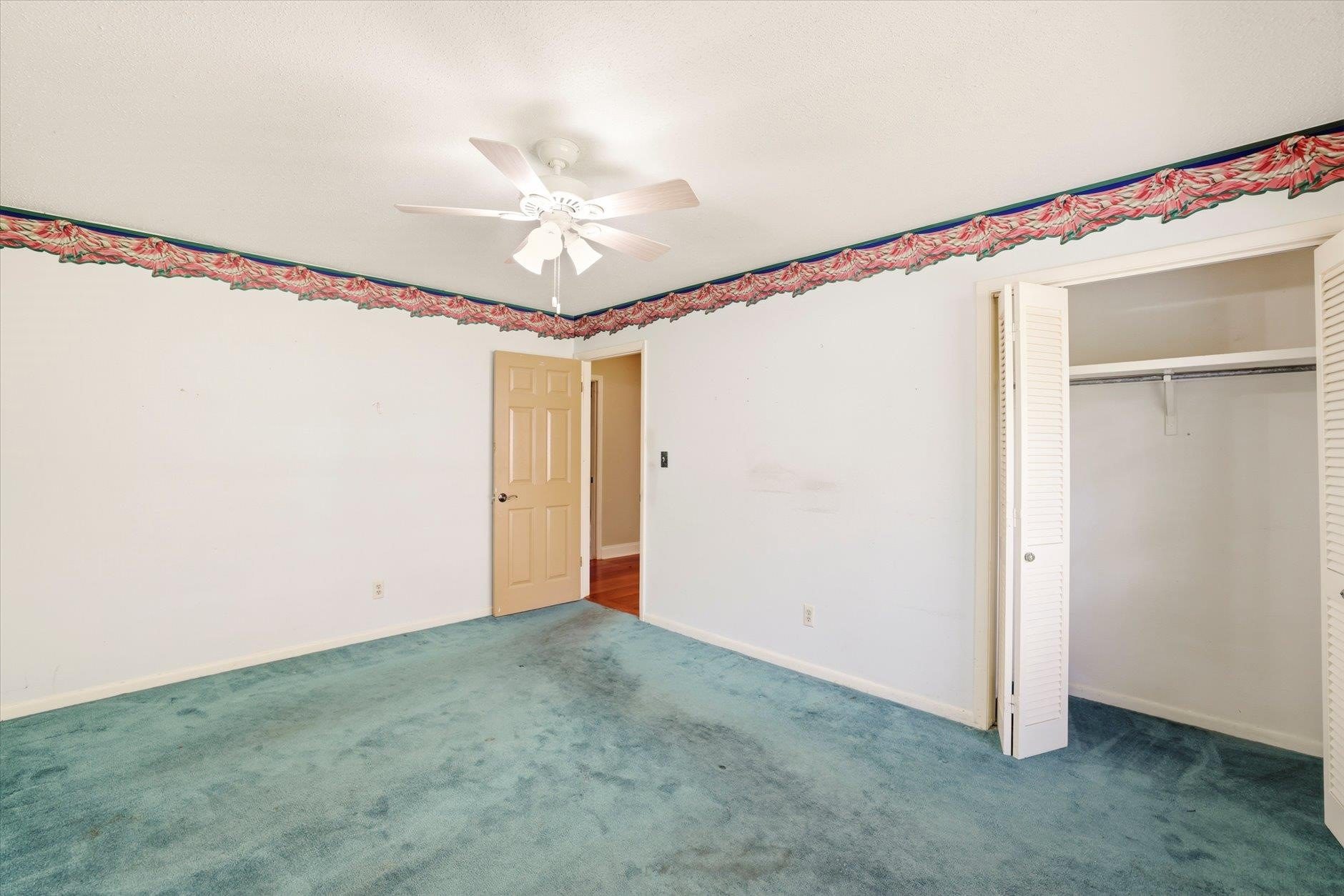 Empty bedroom with green carpet and ceiling fan.