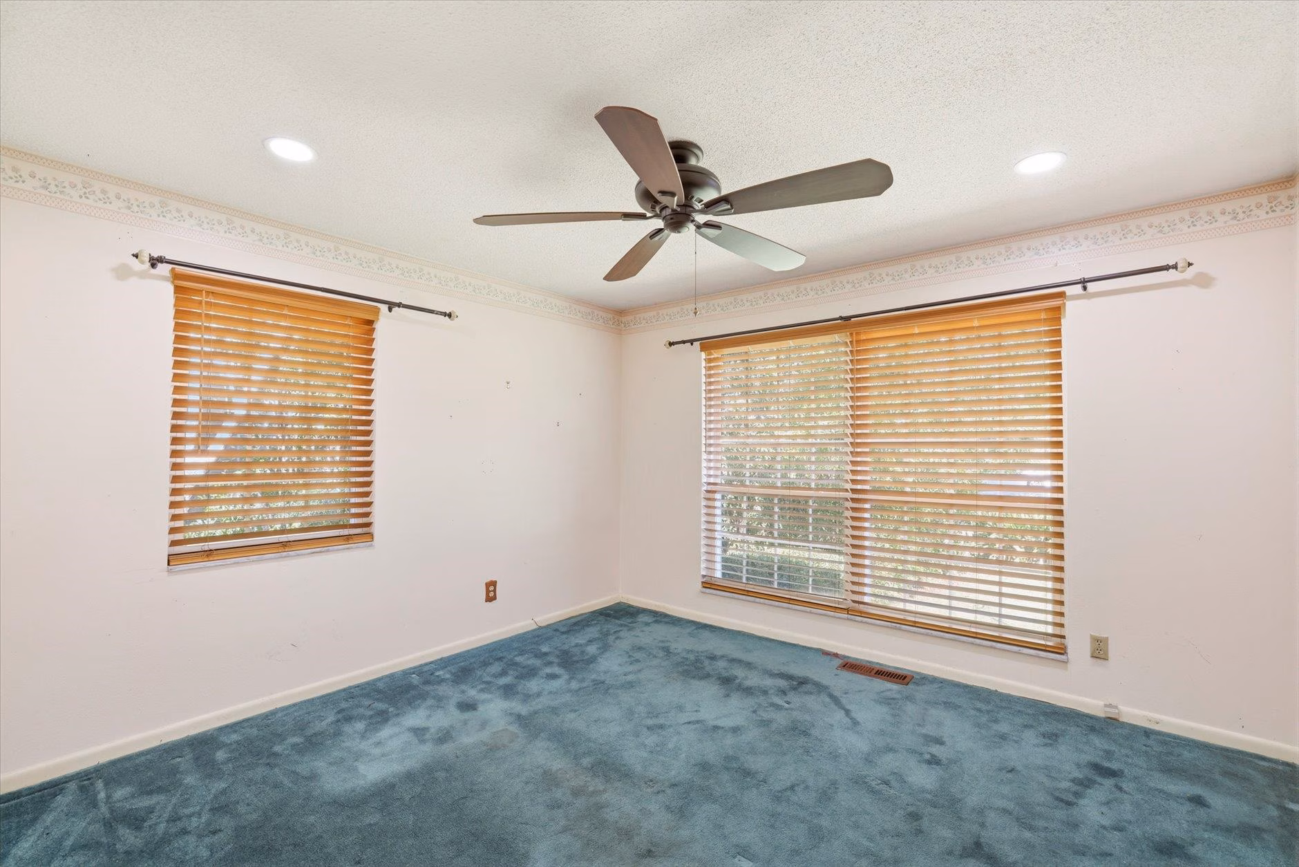 Empty room with blue carpet, ceiling fan, and wooden blinds.