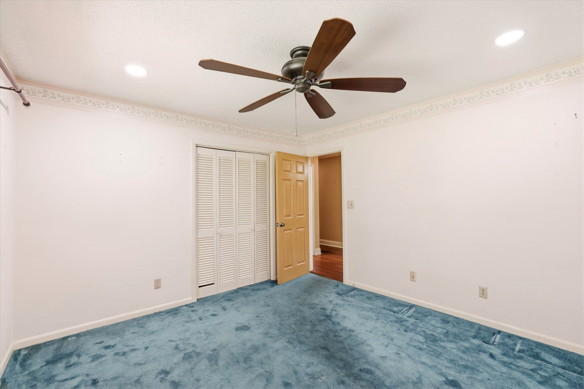 Empty room with blue carpet, white walls, and ceiling fan.