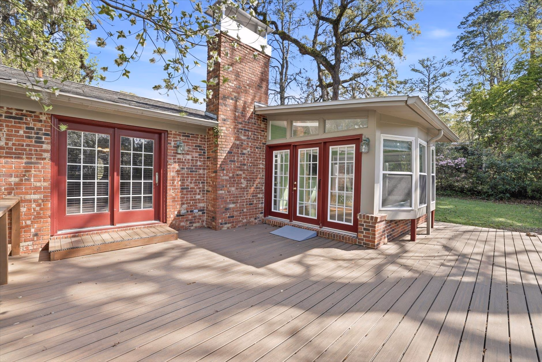 Spacious wooden deck with brick chimney and large red-trimmed windows.