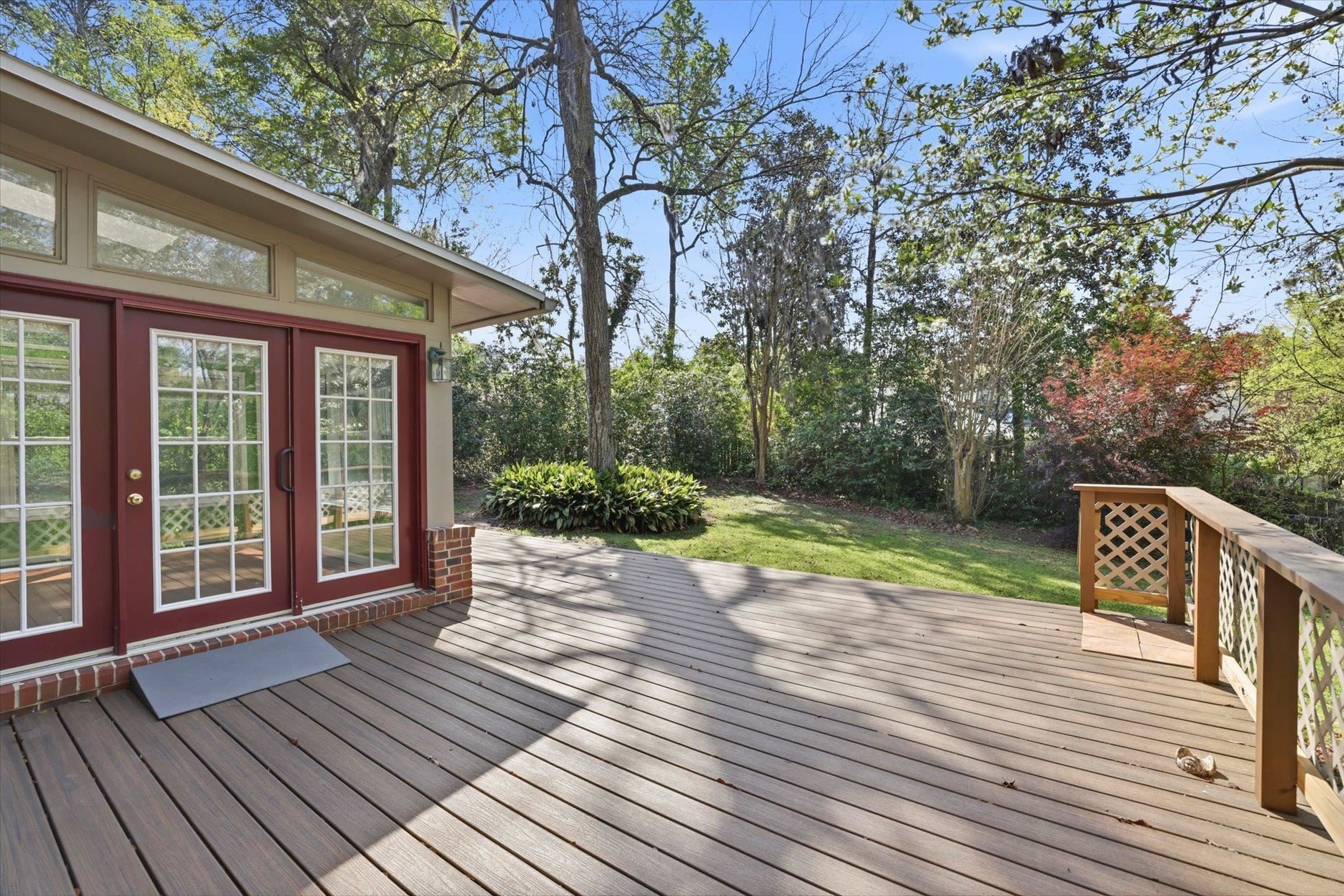 Spacious wooden deck with garden view and glass doors.