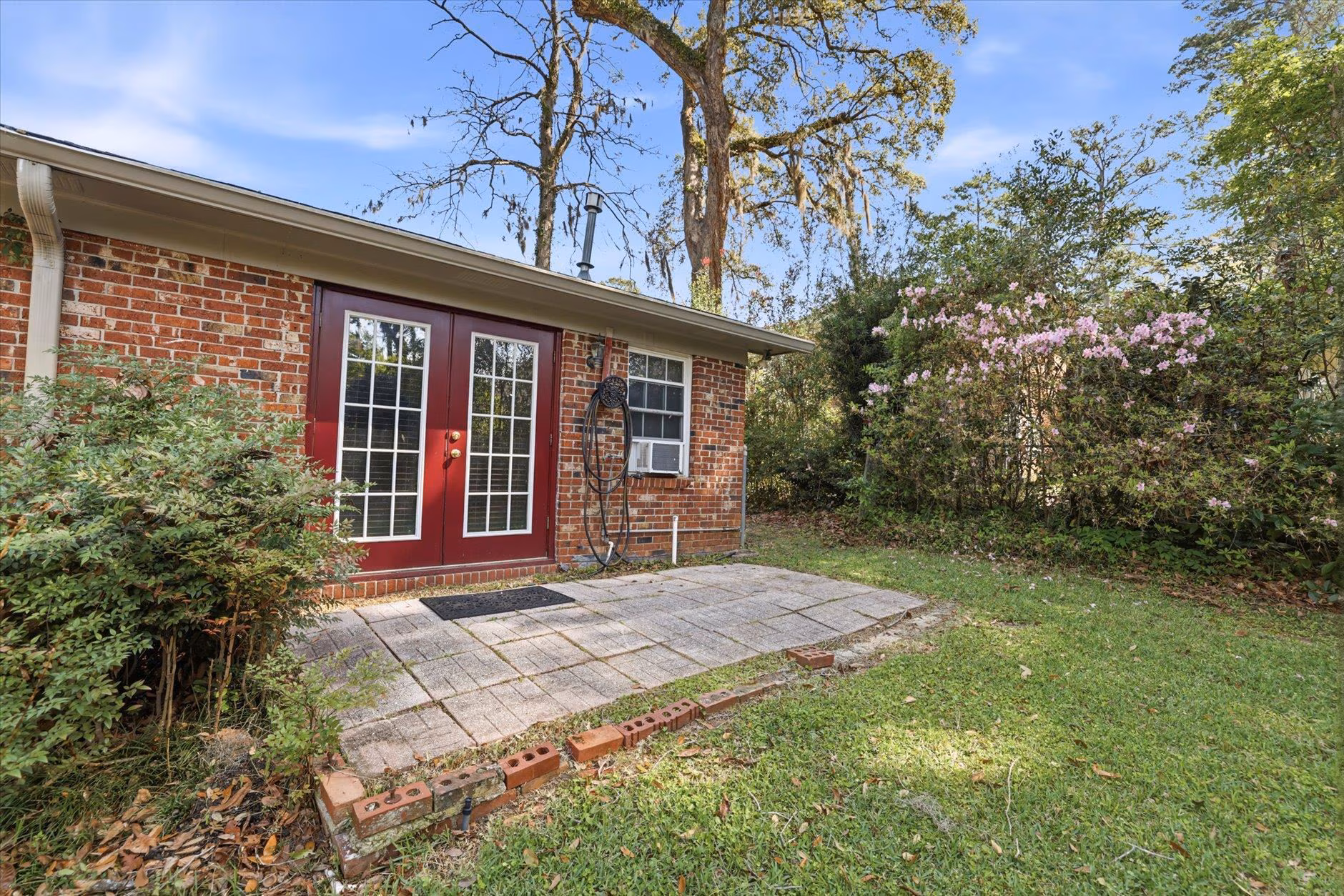 Backyard patio with red French doors and a stone tile floor under a large tree.