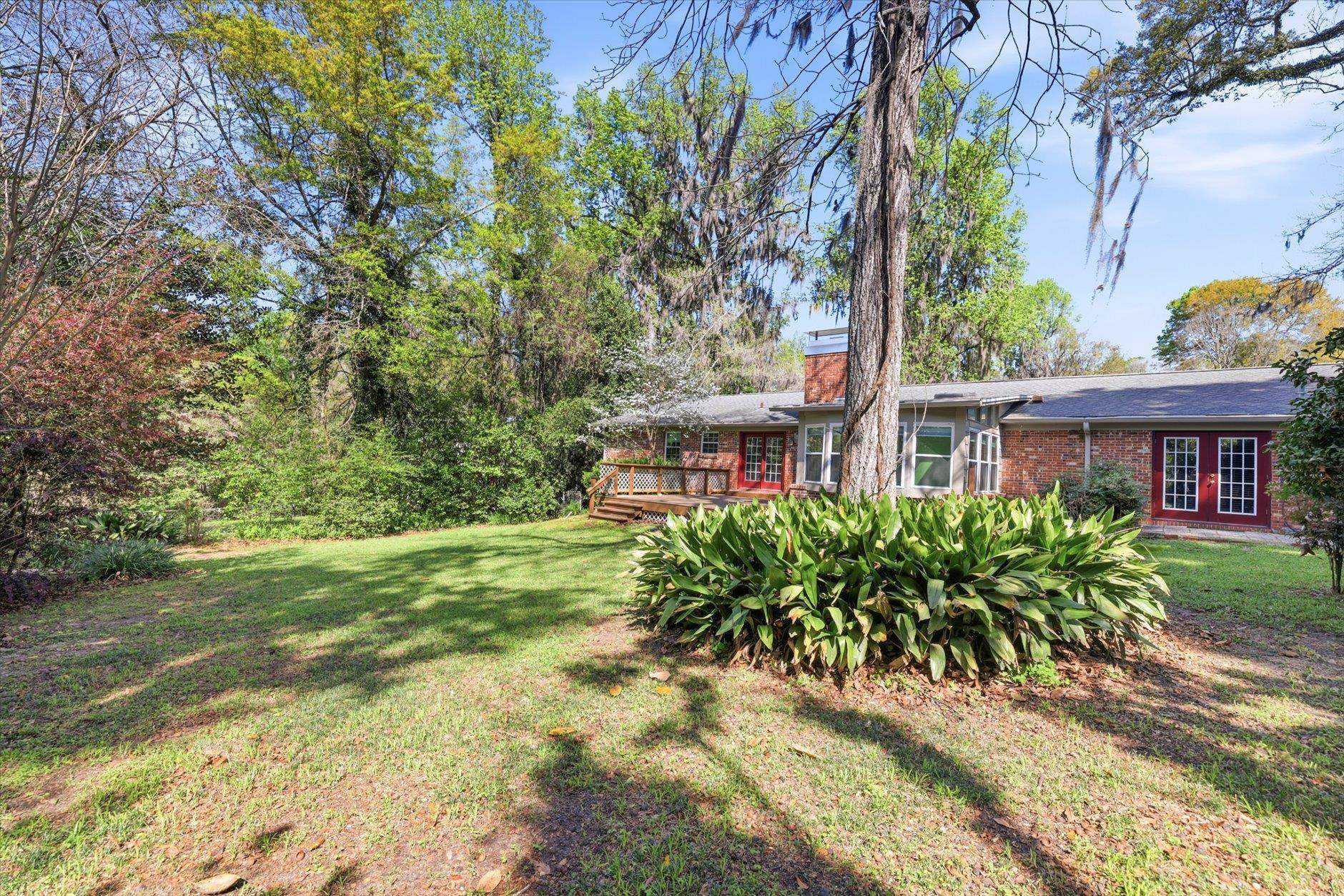 A brick house surrounded by green trees and a grassy yard on a sunny day.