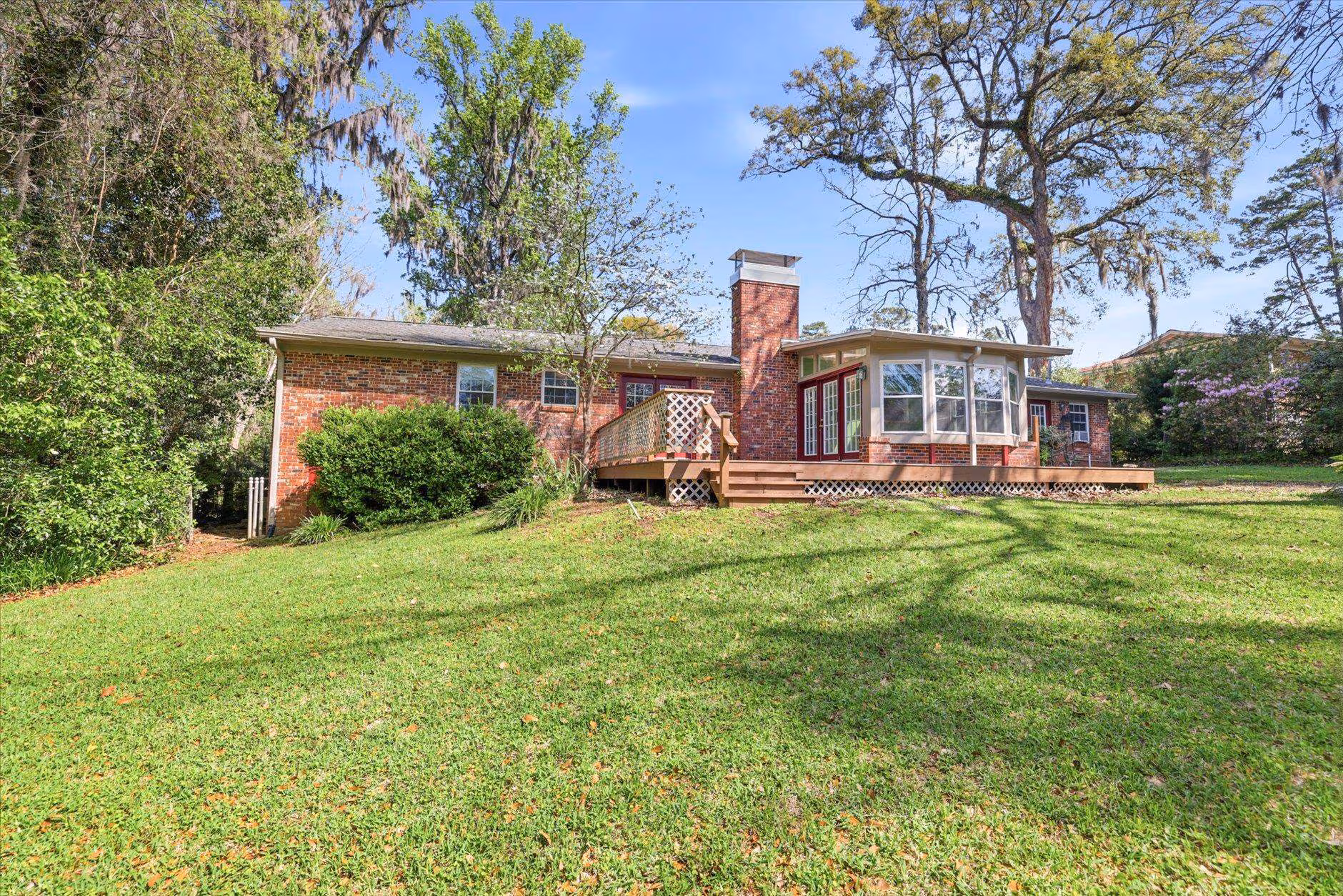 Single-story brick house with a spacious green lawn and tall trees.