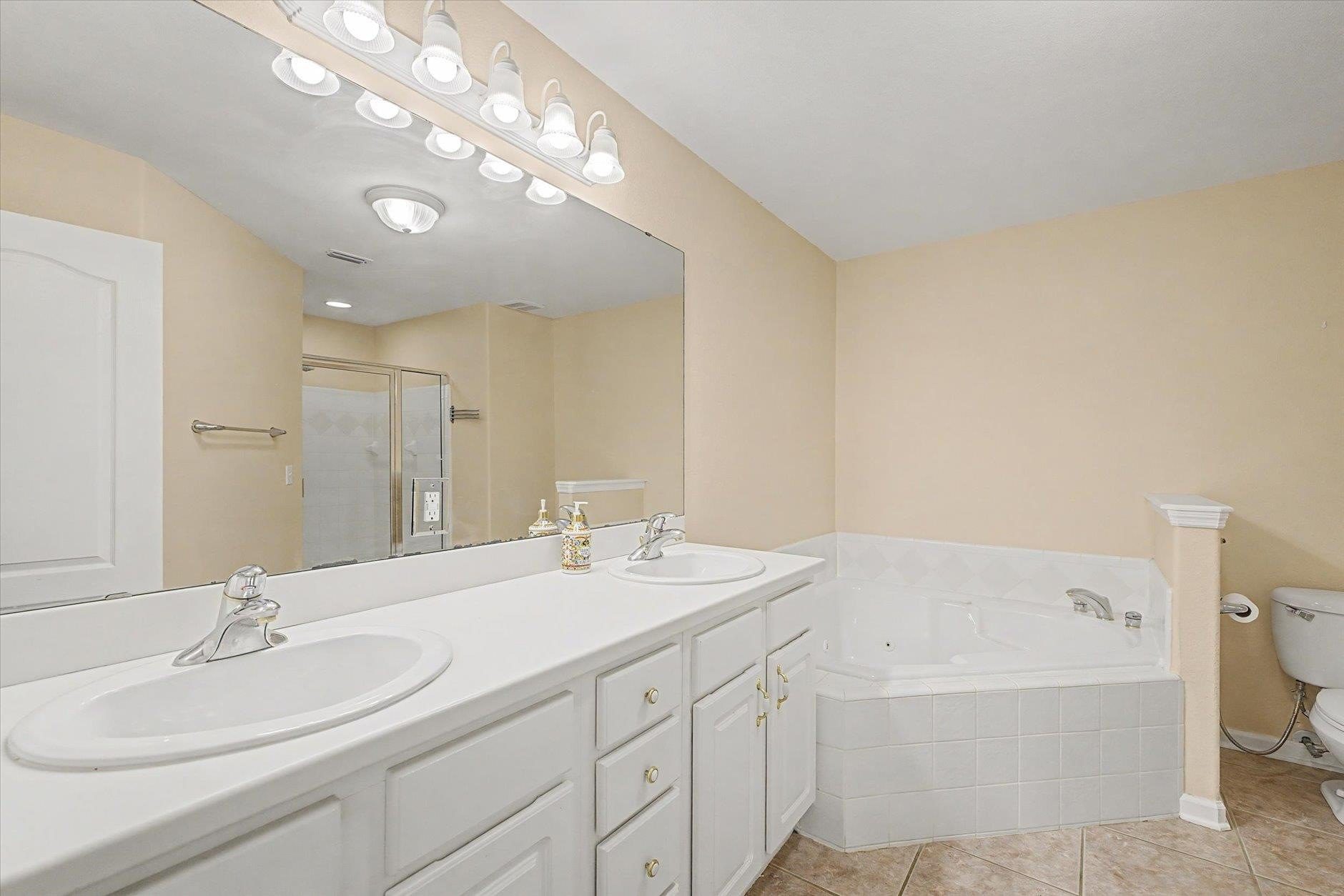 Bright bathroom with white cabinets, dual sinks, and a corner bathtub.