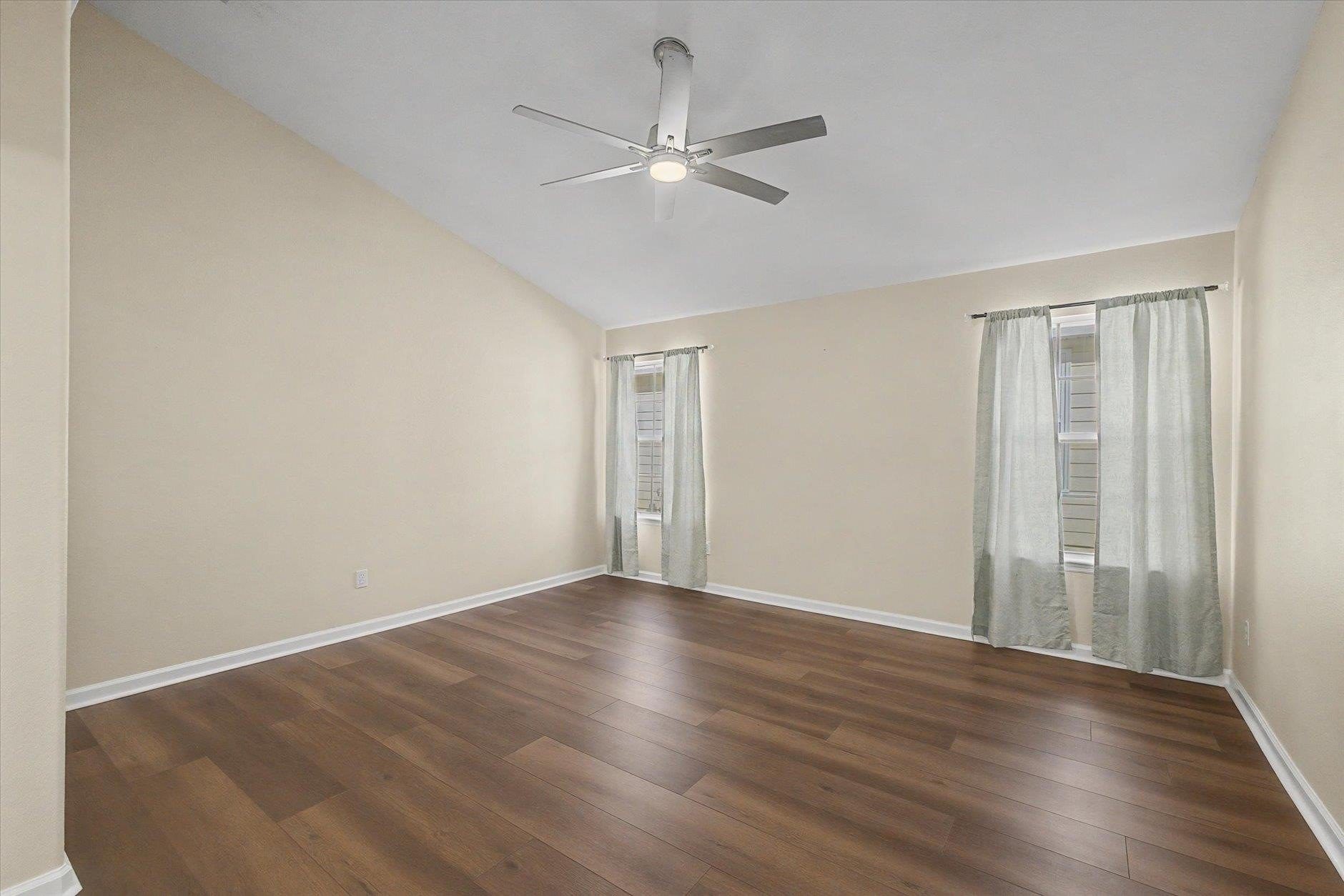 Empty room with wood flooring, beige walls, and ceiling fan.
