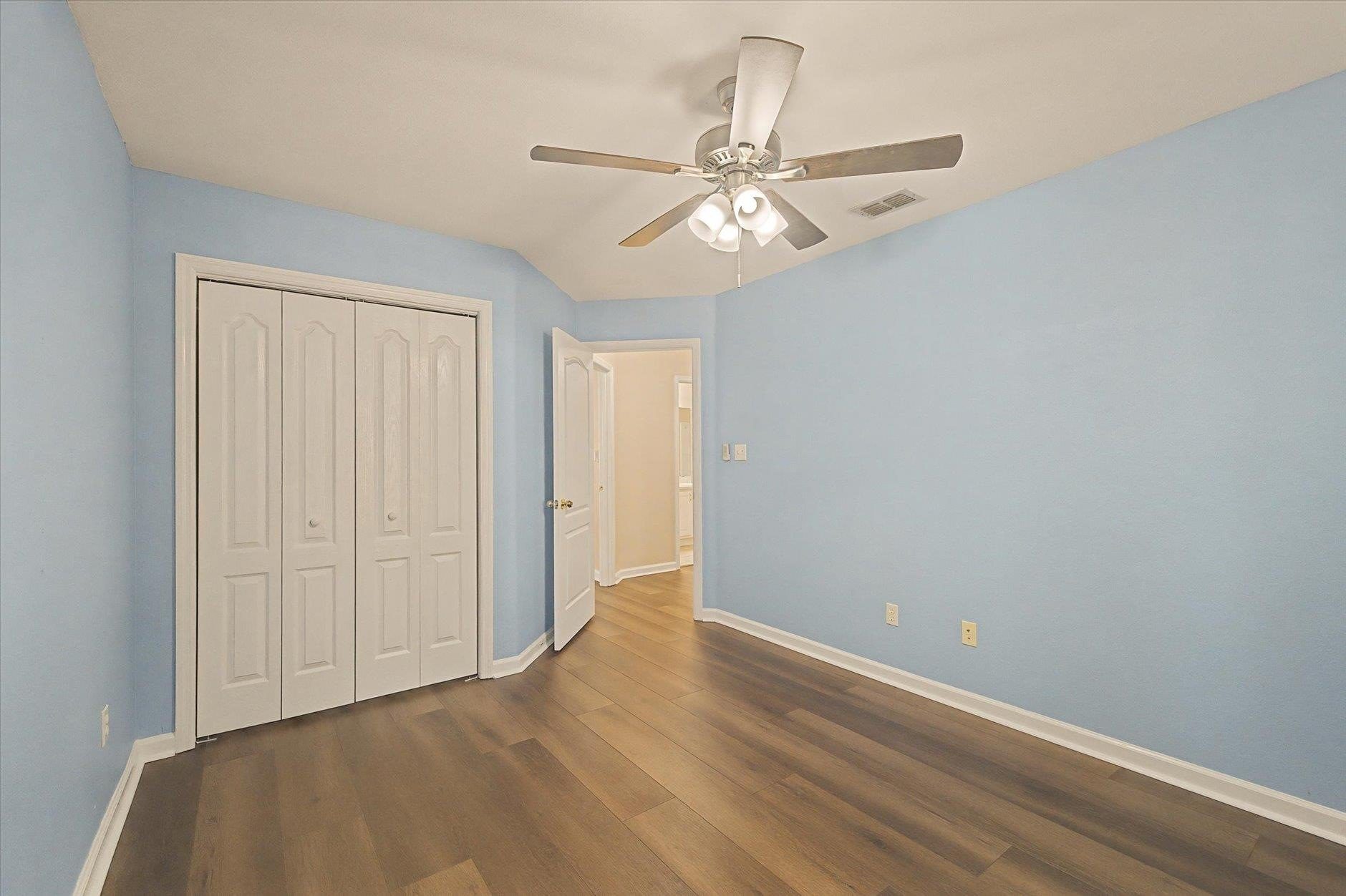 Empty bedroom with blue walls, hardwood floor, and ceiling fan.