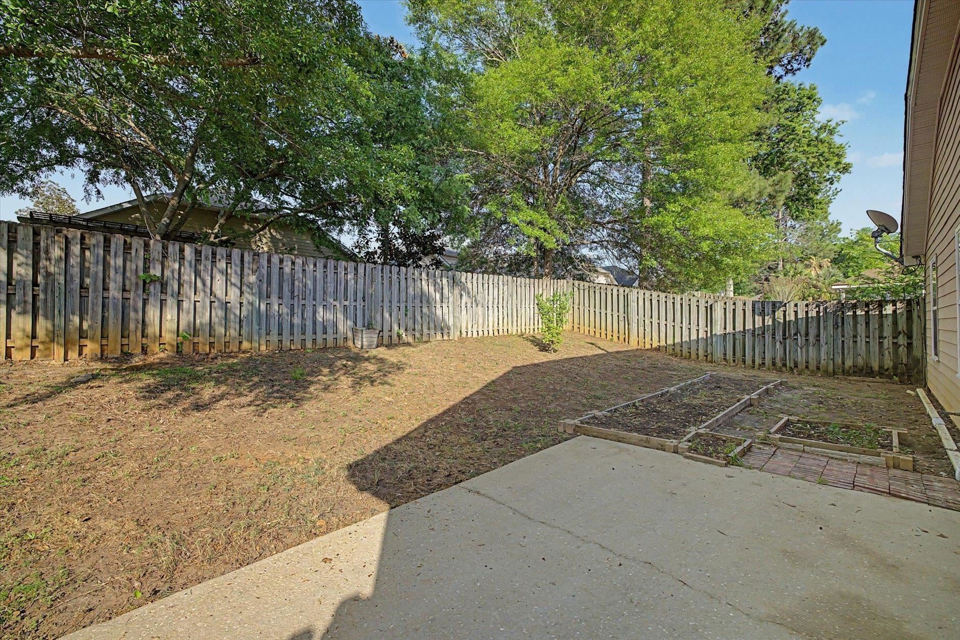 A fenced backyard with trees and a concrete patio.