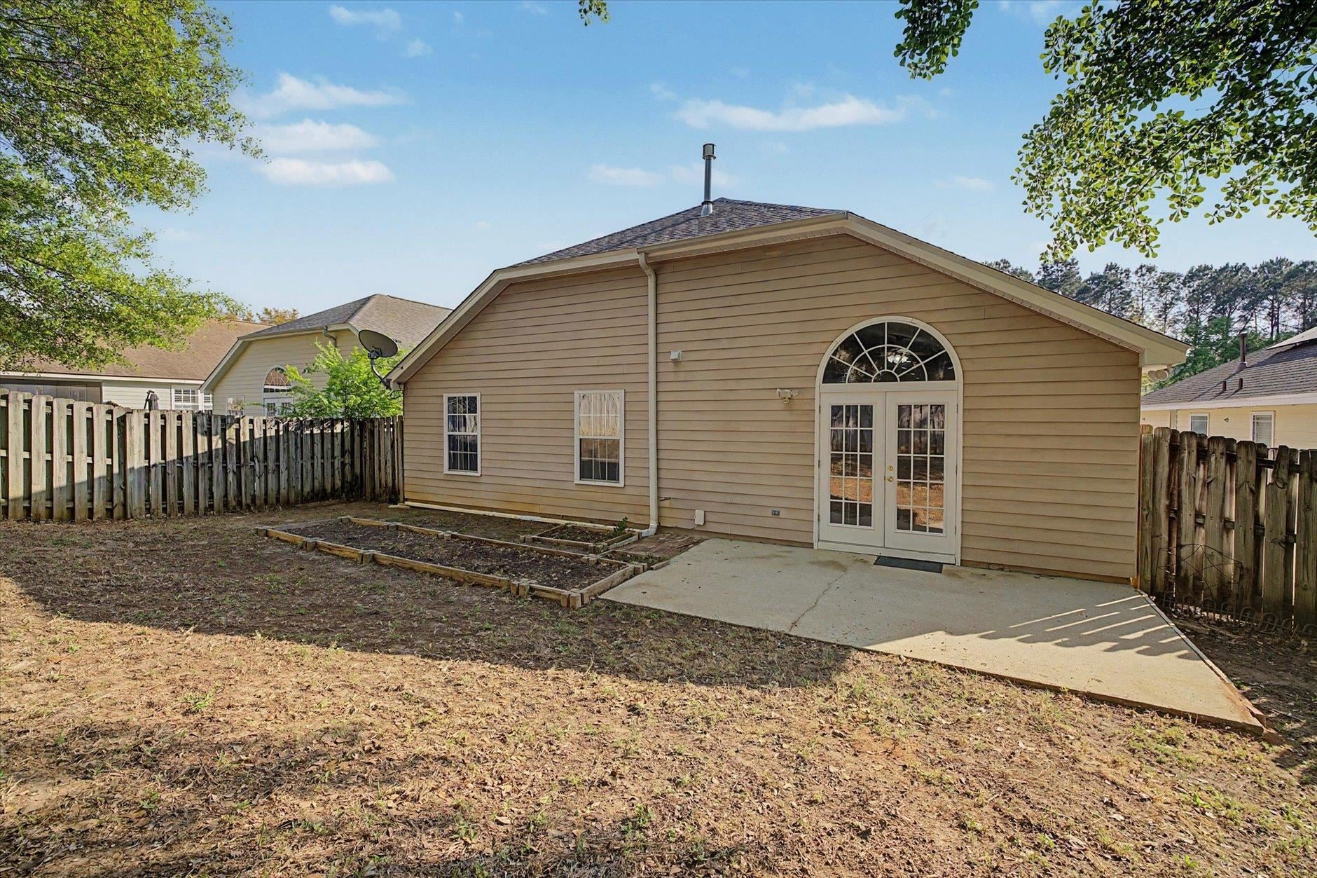 Backyard patio with wooden deck and arched double doors on a beige house.