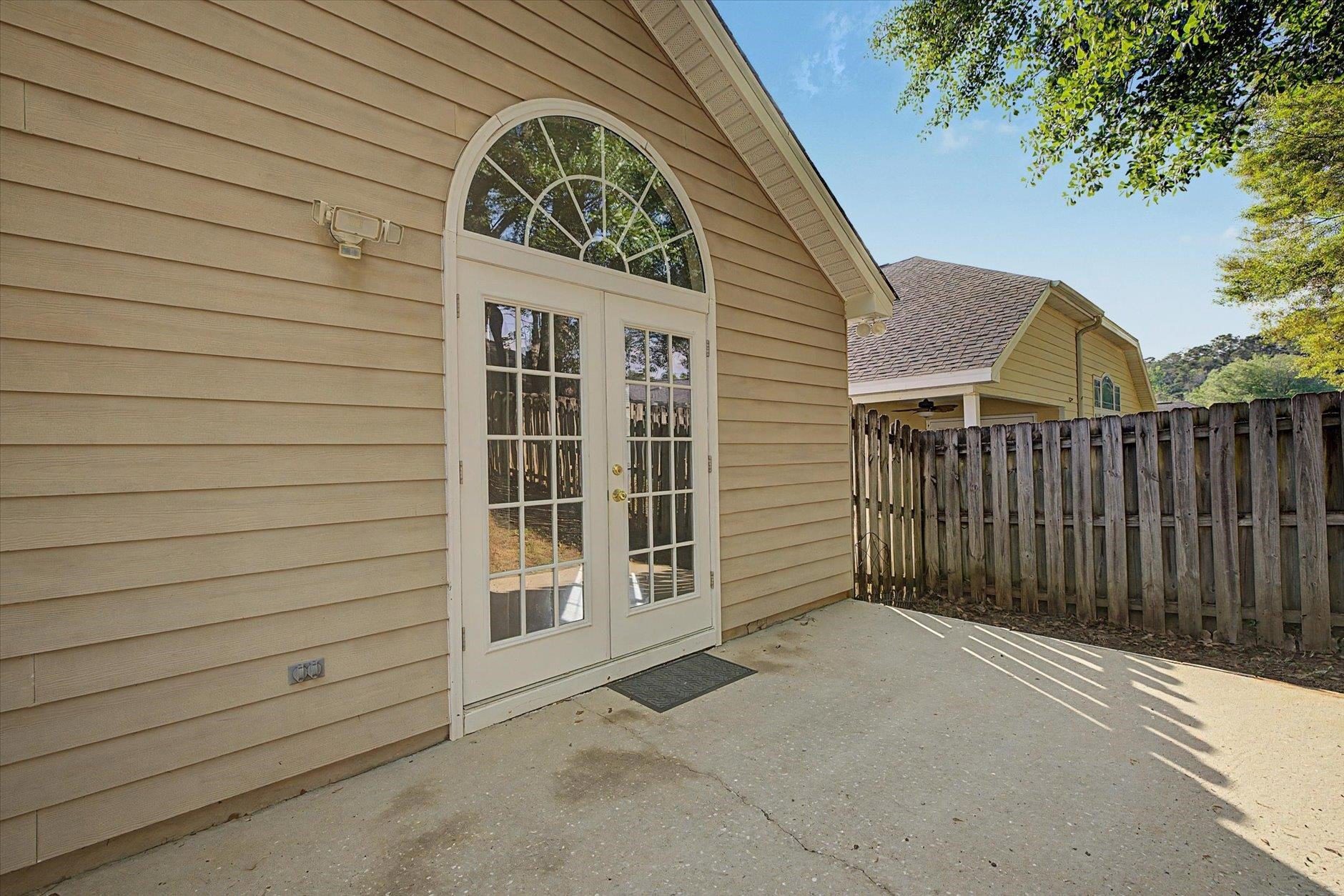Concrete patio outside a beige house with French doors and a privacy fence.