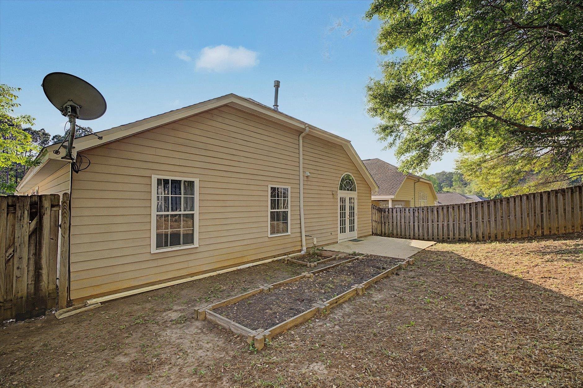 Backyard of a beige house with a small garden bed and fenced yard.