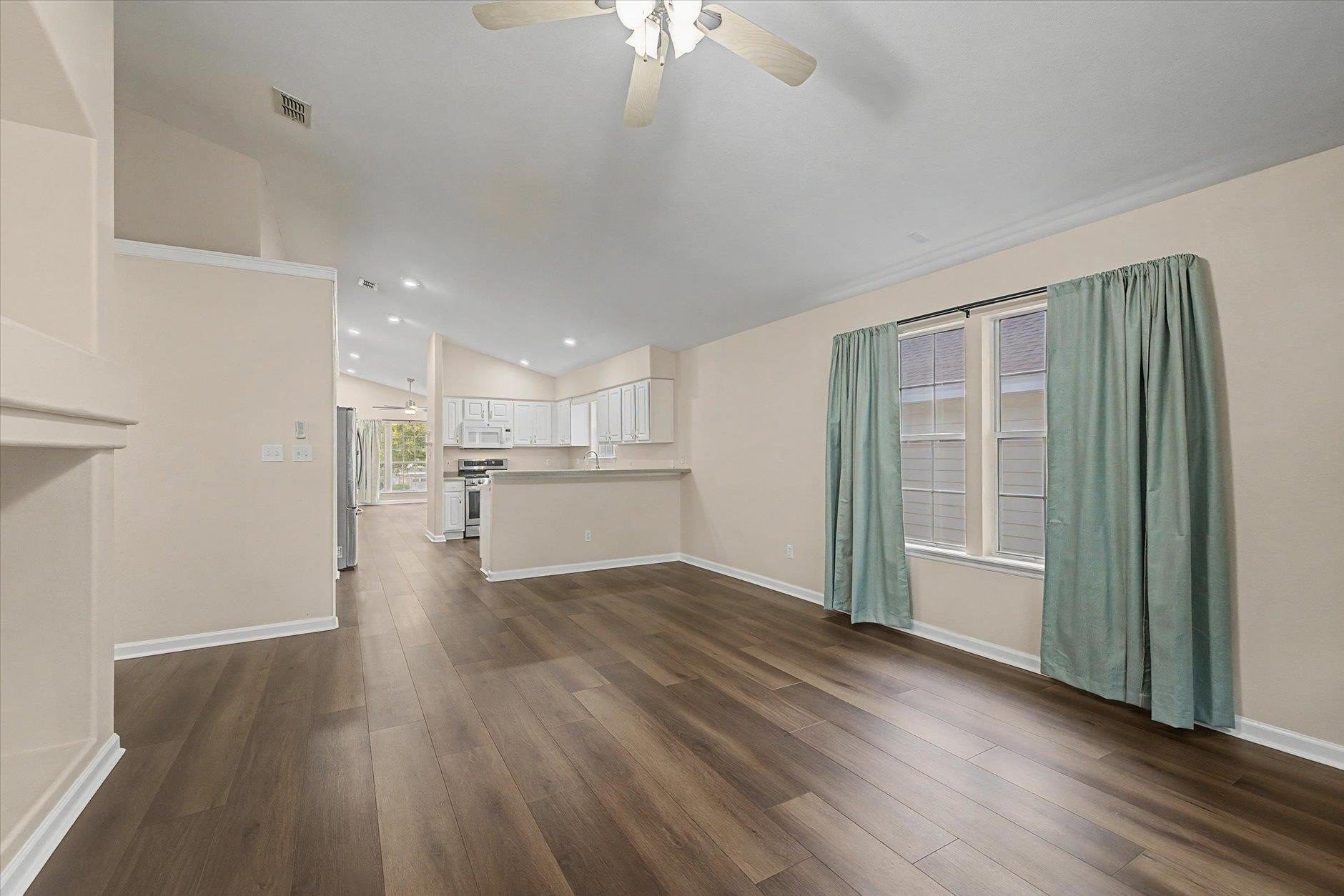 Spacious empty room with wood flooring and large window curtains.