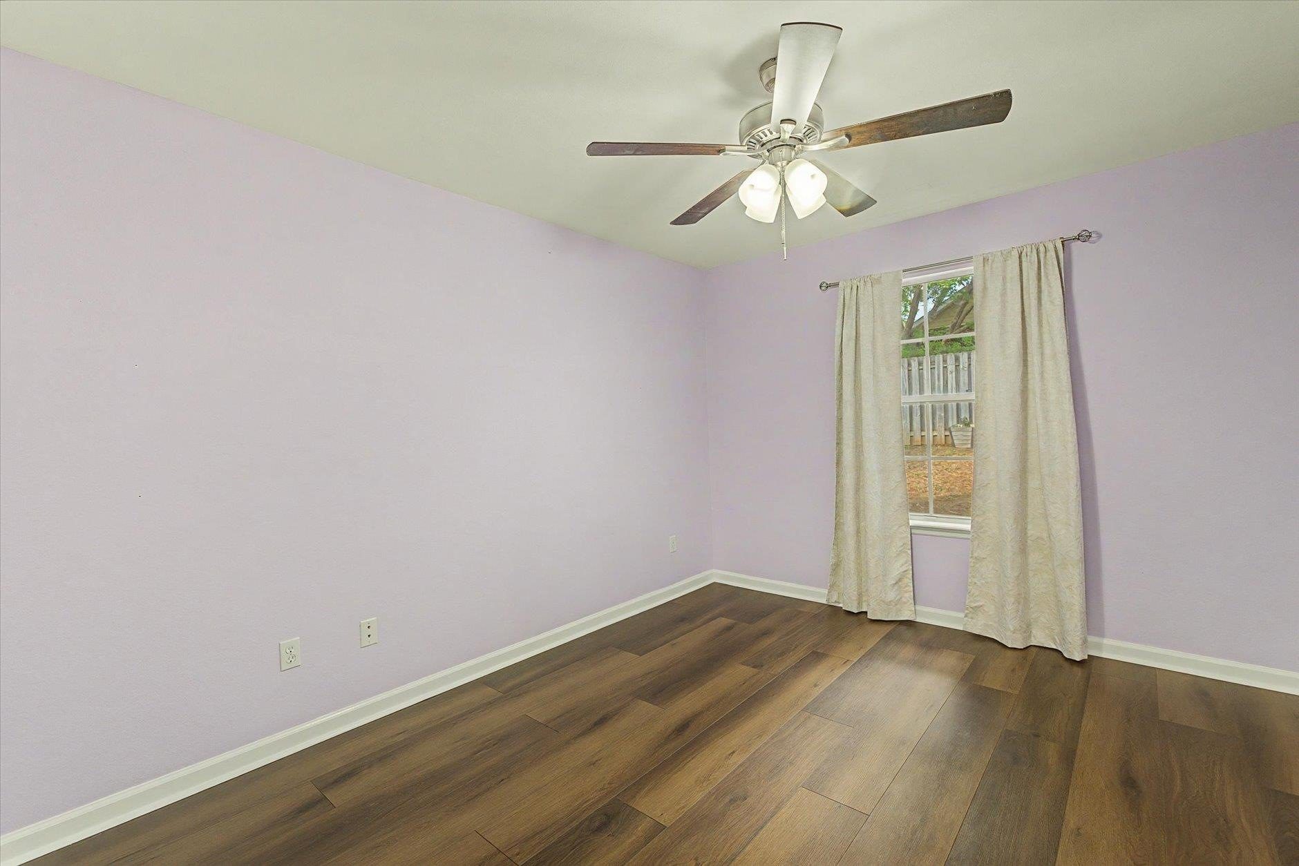 Empty room with light purple walls and wooden floor under ceiling fan.