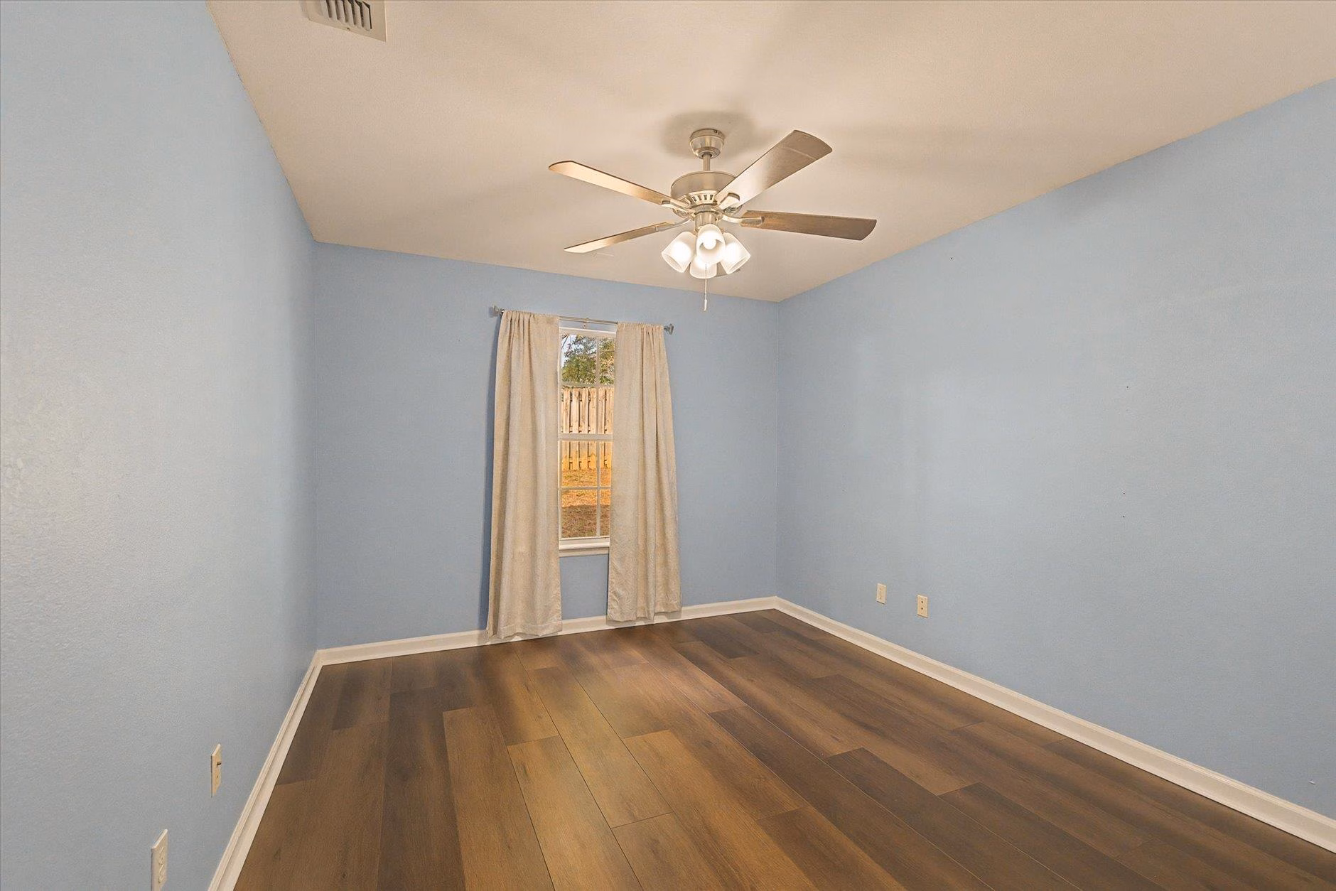 Empty bedroom with light blue walls and wooden floor.
